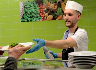 #Mensarevolution – Wie nachhaltig sind Hamburgs Kantinen? Ein junger Mann gibt in einer Mensa Essen aus.