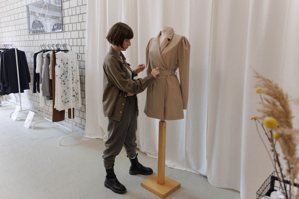 Alina Klemm zupft ein Blazerkleid an einer Modepuppe in ihrem Pop-Up-Store zurecht.