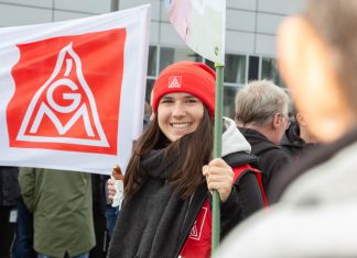 Gewerkschaft ruft Metaller im Norden erneut zu Warnstreik auf Eine Arbeitnehmerin beim Streik hält eine IG Metall-Flagge und lächelt in die Kamera. Foto: Hergen Deuter