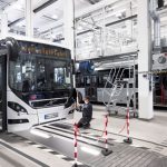 Neues Assistenzsystem der VHH-Busse schützt Radler und Fußgänger Die Buswerkstatt ist hell beleuchtet und mehrere Arbeiter reparieren einen Bus.