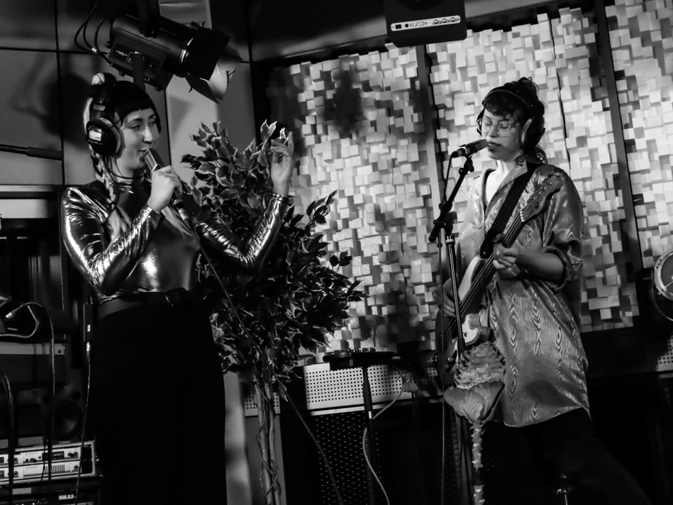 Aulyla bei Mute Solo im Tonlabor. Foto: Sarah Cüpper/Mirjam Bär. Auf dem Bild sieht man zwei Frauen,beide singen in ein Mikrofon, eine spielt außerdem noch Bass.