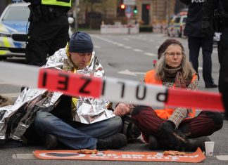 Was nervt, kann trotzdem wirken Zwei Protestierende sitzen auf der Straße, davor Polizeiabsperrband