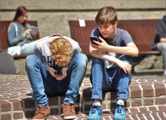 Offene Kinder- und Jugendarbeit ist wichtig Zwei Jugendliche sizten auf einer Mauer und haben ihr Smartphone in der Hand. Symboldbild für offene Kinder- und Jugendarbeit in Hamburg
