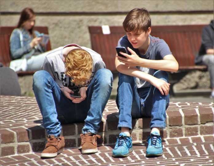 Zwei Jugendliche sizten auf einer Mauer und haben ihr Smartphone in der Hand. Symboldbild für offene Kinder- und Jugendarbeit in Hamburg