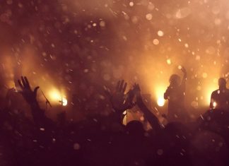 Veranstaltungsbranche – es fehlt an Personal und Ticketverkäufen Eine jubelnde Menschenmenge ist im goldenen Rauch und Lichtermeer zu erkennen.