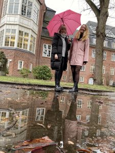 Zwei Frauen stehen in Regenjacke und Regenschirm vor einer Pfütze.