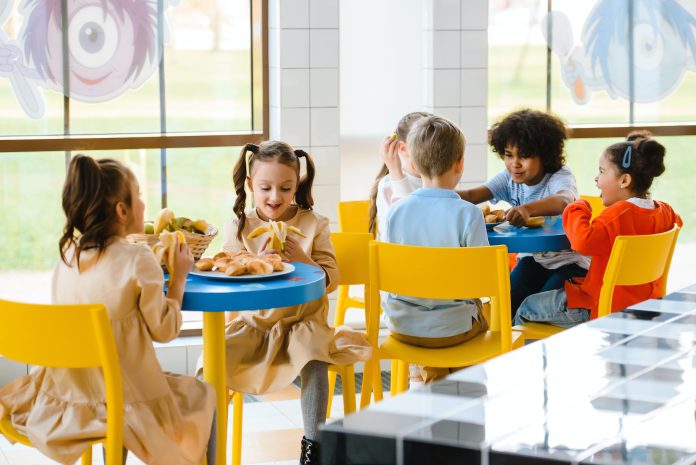Schulverpflegung: Junge Schülerinnen und Schüler sitzen an zwei Runden Tischen und essen.