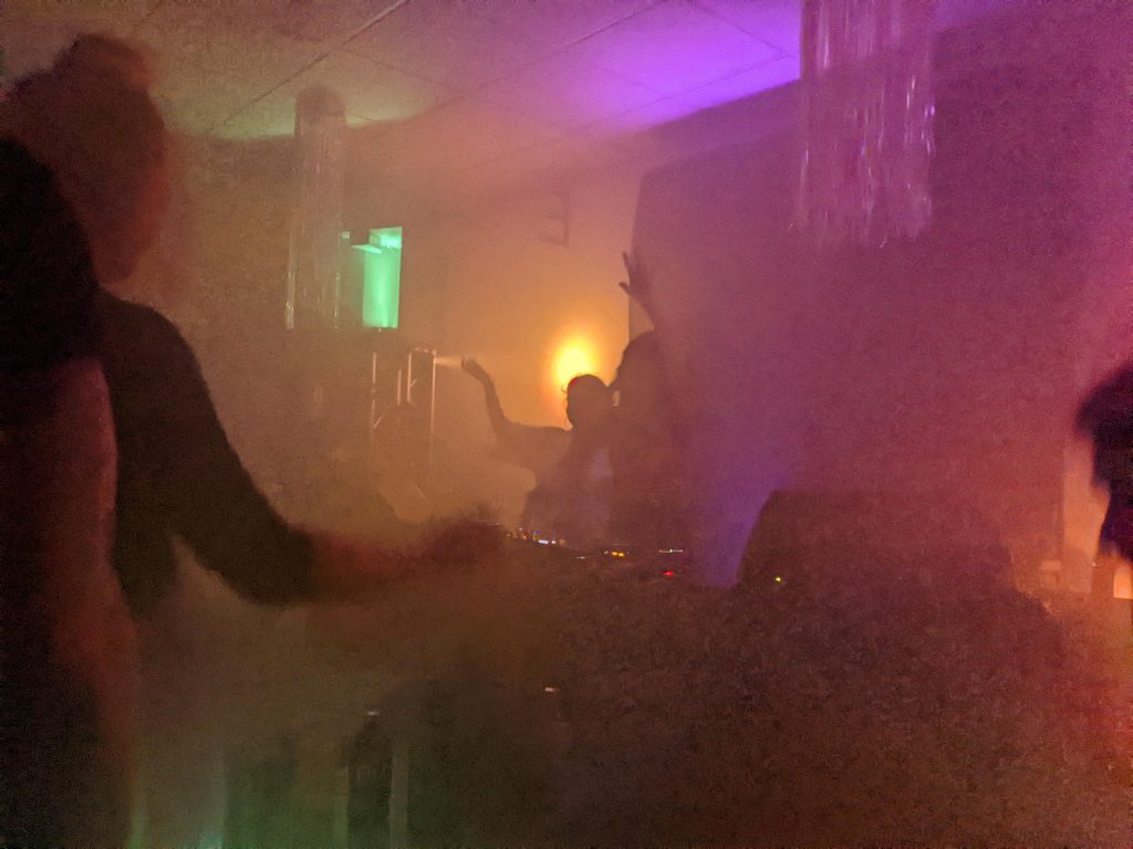 In einer Off-Location spielen die DJs Pardis und Bärbel in Solidarität mit den Protestierenden in Iran. Durch den Nebel beleuchten bunte Lichter die zwei DJs hinter dem Pult.Foto: Francine Sucgang
