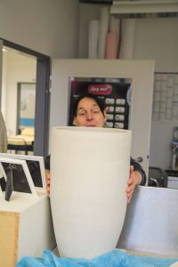 Eine Werkstatt-Mitarbeiterin steht hinter einen großen, weißen Keramik-Schüssel.