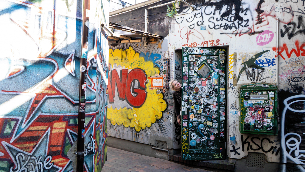 Eine Frau steht im Eingang einer und lässt ihren Kopf rausragen, um sie herum ist Graffiti