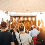Tipps für ein sonniges Wochenende im Juni Festivalbesucher*innen werden bei Sonnenschein von hinten fotografiert mit dem Gesicht zur Bühne.