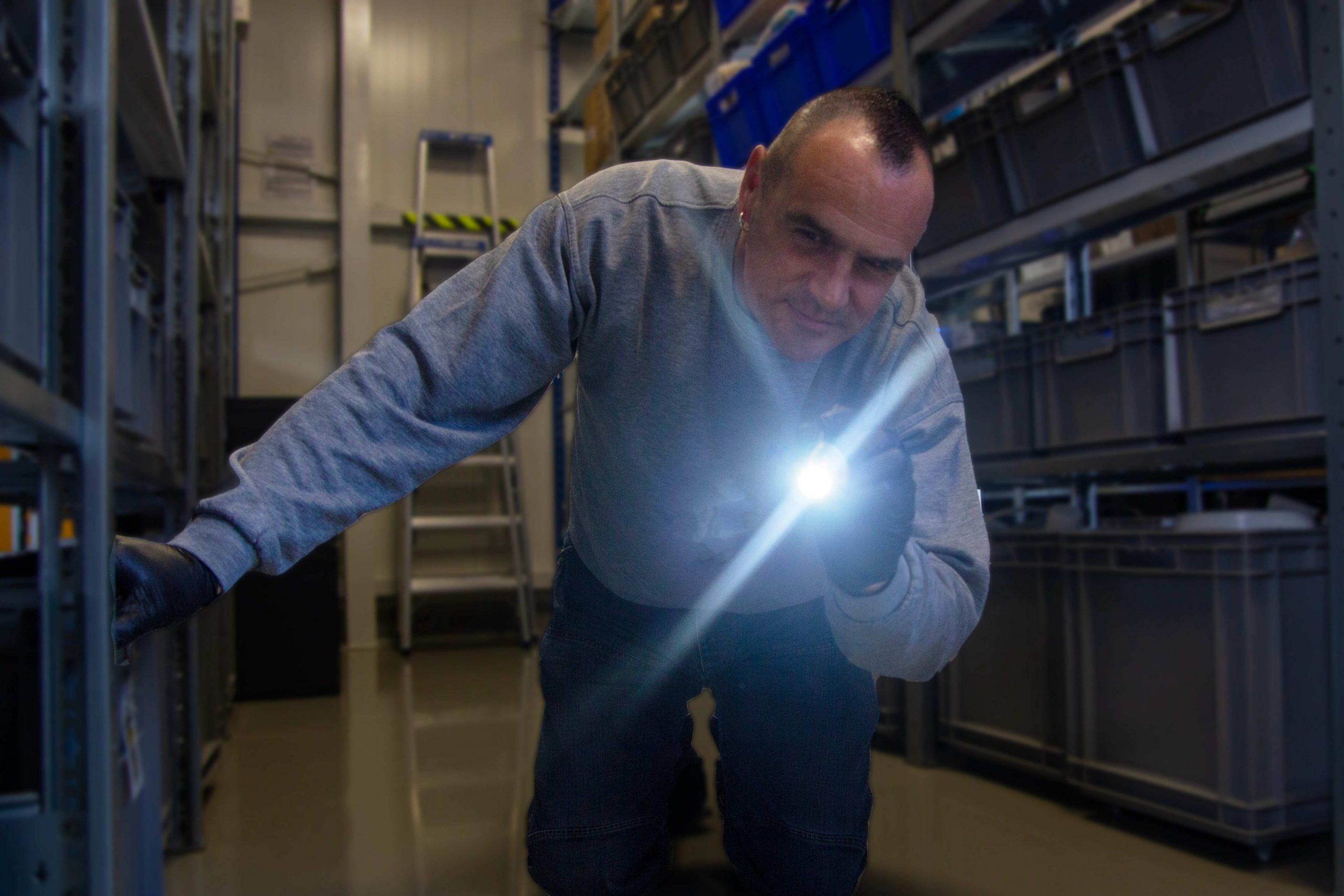 Schädlingsbekämpfer Dennis Kalff leuchtet mit einer Taschenlampe unter ein Regal