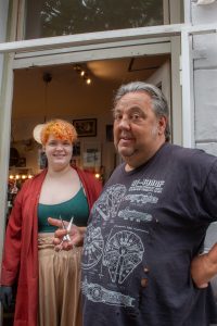 Zwei Personen vor einem Friseursalon. Mit einer Schere in der Hand. 