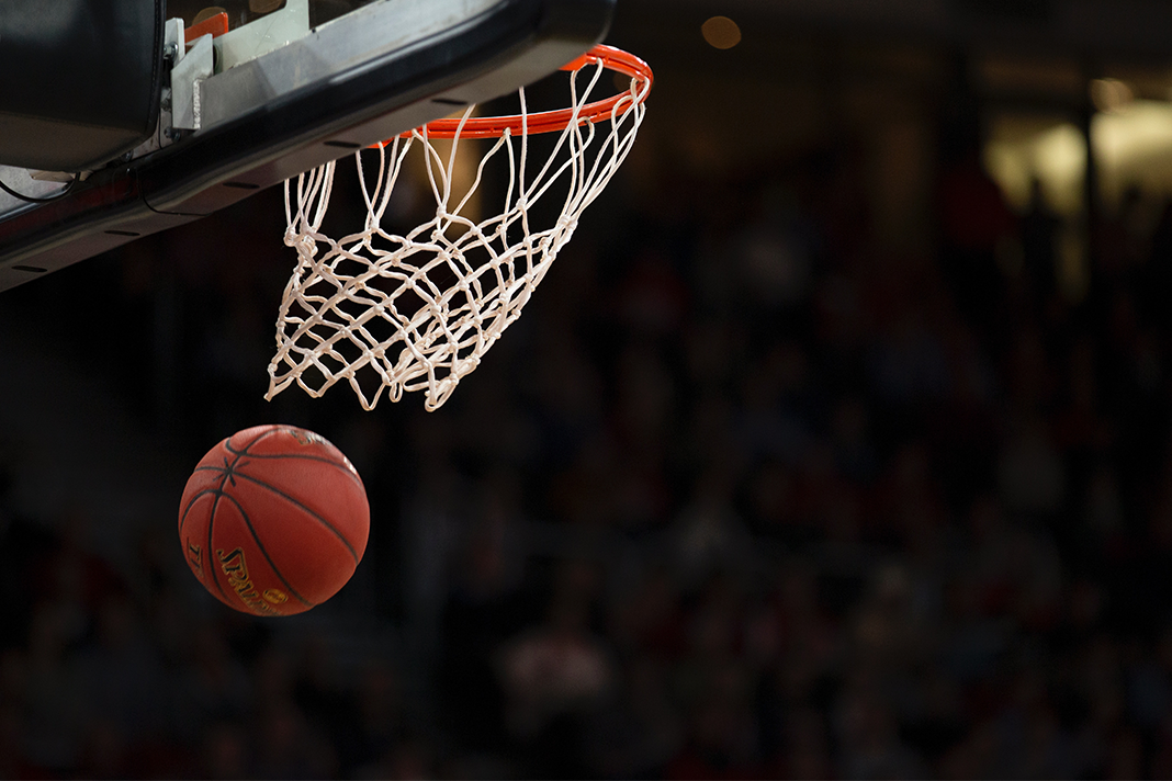 Es ist ein Basketballkorb zu erkennen. Der Ball fliegt durch das Netz vom Korb.