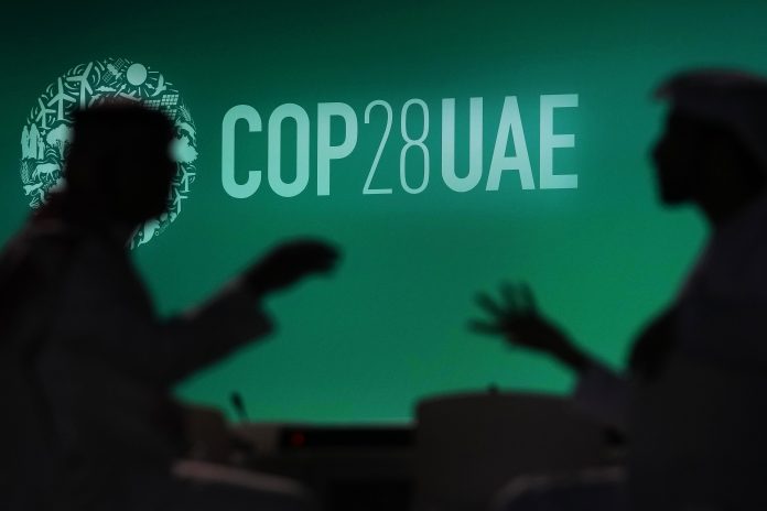 Zwei Menschen unterhalten sich vor einem Logo des UN-Klimagipfels COP28. Bei dem COP28-Treffen wollen mehr als 190 Länder ab Donnerstag am Persischen Golf die erste große Bestandsaufnahme der Umsetzung der Pariser Klimakonferenz 2015 erstellen.