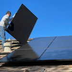 Bürgerschaft stimmt neuem Klimaschutzgesetz zu Klimaschutzgesetz Hamburg: Mann in weißem Hemd und blauer Jeans sitzt auf weißem und schwarzem Solarpanel.