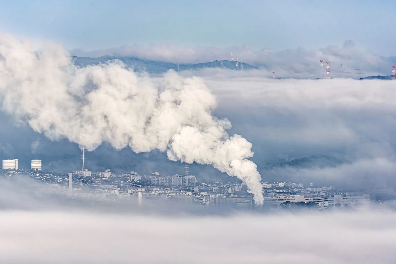 Panorama von einer Stadt in den Bergen mit einer Fabrik, die Rauch ausstößt.