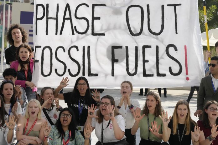 COP28 Protest gegen Fossile Brennstoffe: Aktivisten demonstrieren mit einem Schild mit der Aufschrift 