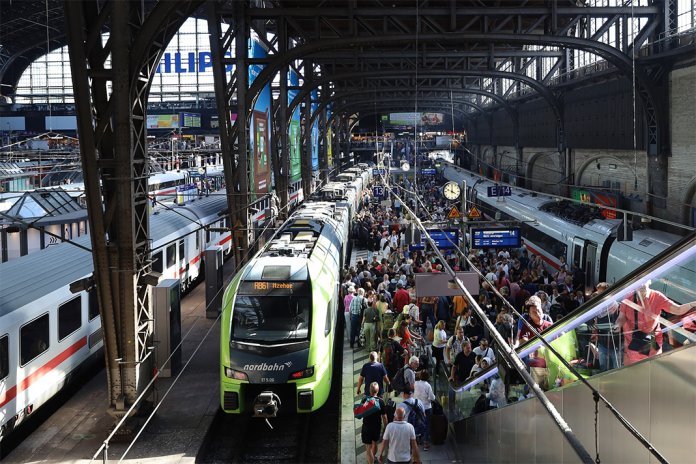 Ein grüner Zug steht an einem Gleis im Hamburger Hauptbahnhof. Auf dem Gleis stehen viele Menschen.