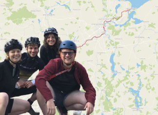 Mit dem Fahrrad an die Ostsee Im Hintergrund eine Karte mit rot eingezeichneter Route von Hamburg nach Travemünde. Im Vordergrund unten links im Bild eine Gruppe von vier jungen Menschen in Fahrradklamotten mit Helmen, die in die Hocke gehen.