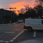 Vorsicht vor Eisglätte und Hochwasser Eine Kreuzung in Hamburg, auf der ein weißes Lieferfahrzeug fährt. Der Himmel ist morgenrot, auf dem Boden sieht man Neuschnee.