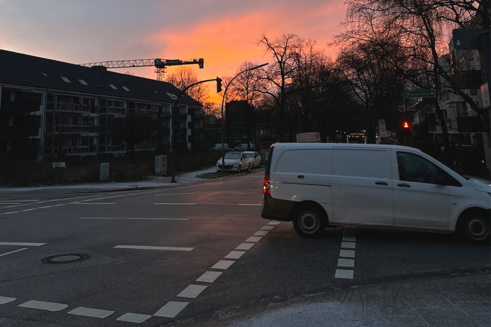 Eine Kreuzung in Hamburg, auf der ein weißes Lieferfahrzeug fährt. Der Himmel ist morgenrot, auf dem Boden sieht man Neuschnee.