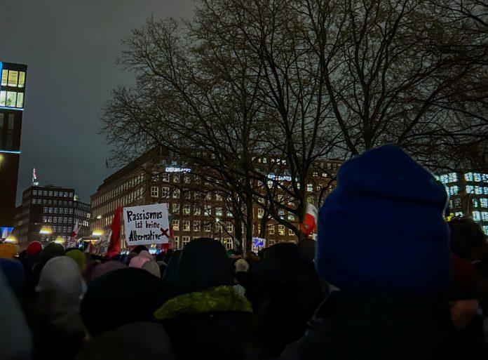Von hinten sind Demonstrierende zu sehen. Auf einem Schild steht: Rassismus ist keine Alternative. Das Foto wurde bei einer vergangenen Demo gegen Rechts in Hamburg aufgenommen.