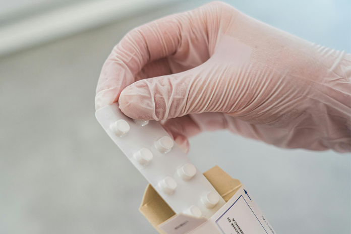 Symbolbild Corona-Medikament Paxlovid: Eine Hand in durchsichtigem Handschuh zieht einen Pillenblister aus einer Medikamentenverpackung.