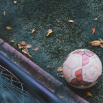 Baller League: Das musst du über die neue Fußballiga wissen Ein Fußball liegt auf dem Boden vom einem Kunstrasenfußballplatz. Ein paar braune BLätter von einem baum liegen auf dem Boden, um den Ball herum und ein Geländer ist zu sehen. Das Bild ist aus der Vogelperspektive aufgenommen.