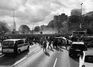 Neuer Prozess zu Ausschreitungen beim G20-Gipfel Das schwarz-weiß Bild zeigt eine Demonstration zum G20-Gipfel in Hamburg mit Polizeiautos und Polizisten.