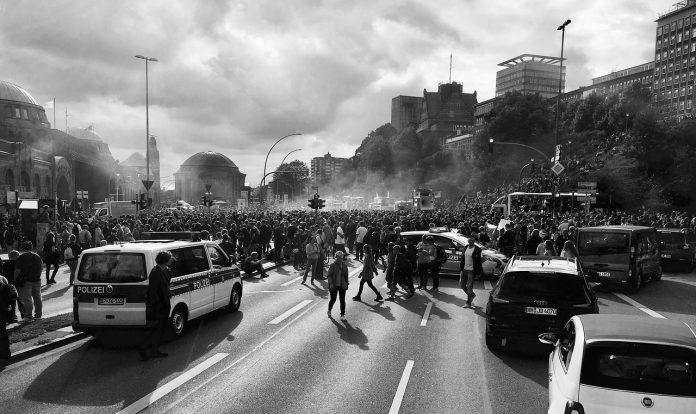 Das schwarz-weiß Bild zeigt eine Demonstration zum G20-Gipfel in Hamburg mit Polizeiautos und Polizisten.