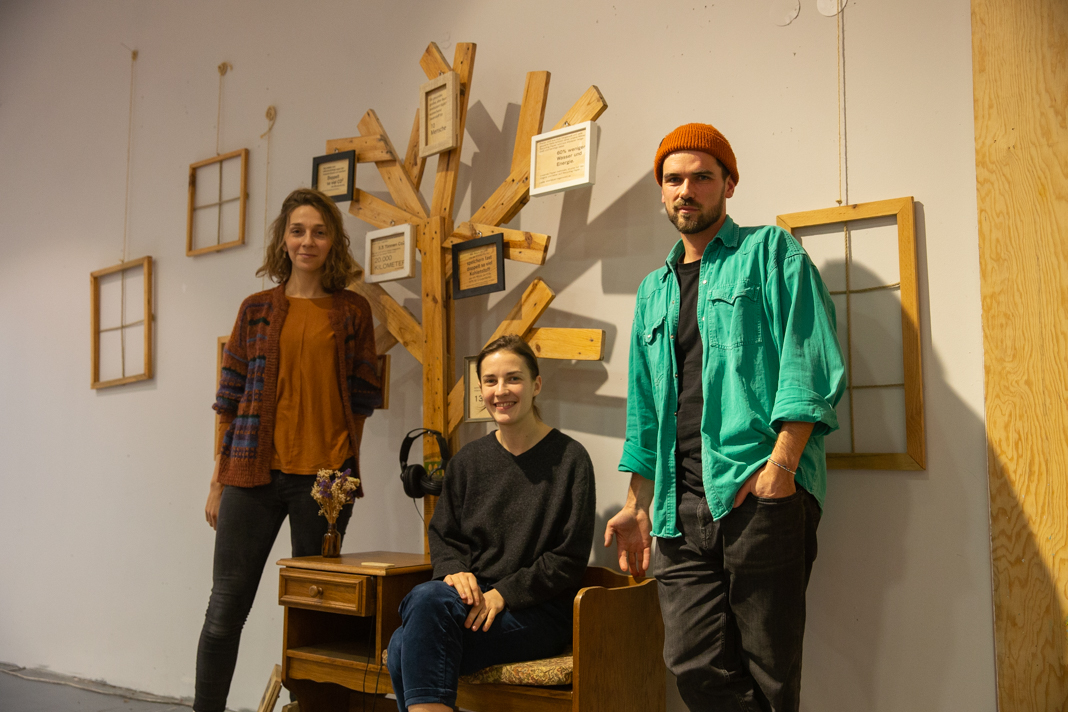 Das Team von Zelt17 steht vor einem ihrer Ausstellungsstücke: ein Holzbaum mit beschrifteten Bildern.