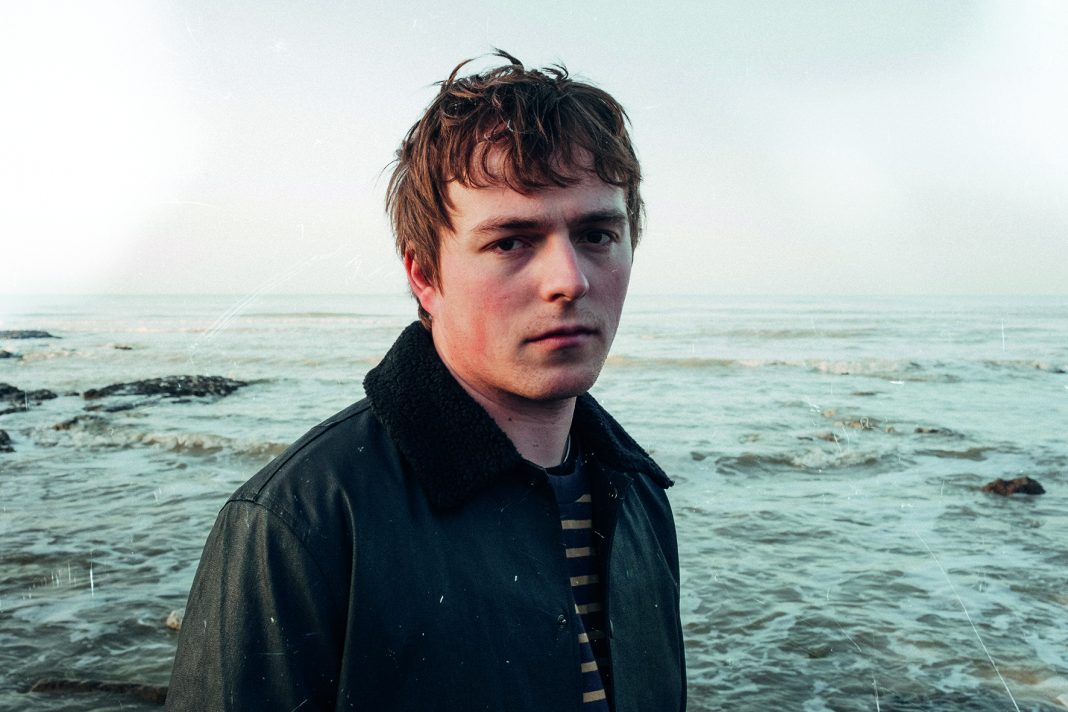 Der Singer-Songwriter Michèl von Wussow steht in einer schwarzen Jacke am Meer.