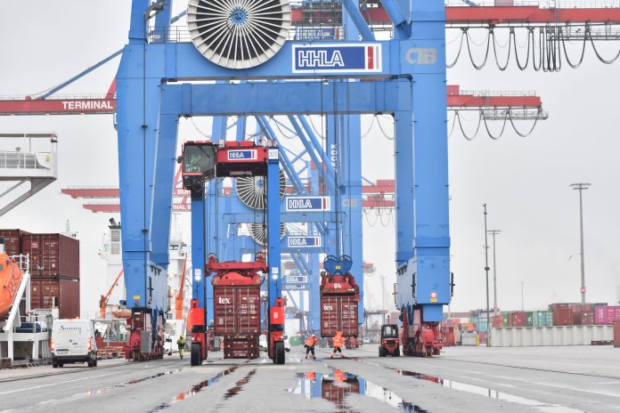 Van Carrier und Brücken im Hamburger Hafen mit Arbeitern und Containern im Hintergrund