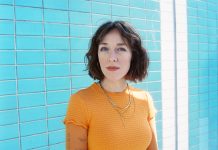 Antje Schomaker: „Leute, ich bin jetzt sexy” Antje Schomaker steht in einem orangenen Oberteil vor blauen Kacheln