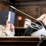 Reichsbürger-Prozess: Die bizarren Pläne der „Kaiserreichsgruppe“ Der Angeklagter der Kaiserreichsgruppe sitzt im Verhandlungssaal und verbirgt sein Gesicht hinter einem Ordner.