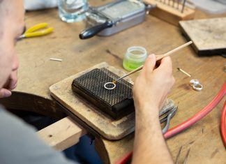 Goldschmieden lernen: Vorlesung mal anders Im Zentrum des Bildes ist ein Ring, der mit Flussmittel bestrichen wird. Im Hintergrund liegen einige Gegenstände herum.