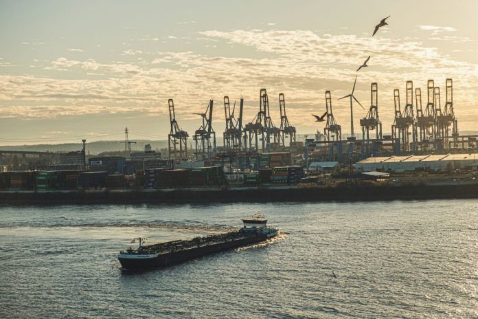 Ein Containerschiff auf der Elbe, im Hintergrund der Hamburger Hafen