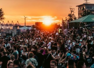 Festivalsommer 2024: Was geht in und um Hamburg? Das Festivalpublikum des MS Dockvill Festivals. Im Hintergrund der Hafen bei Sonnenuntergang.