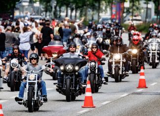 Tattoos und BBQs auf den Hamburg Harley Days 2024 Hamburg Harley Days: Eine Gruppe Motorradfahrer*innen fährt auf einer abgesperrten Straße.