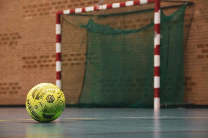 Ein Handball liegt vor einem Handballtor in einer Sporthalle.