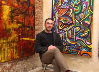 “Kunst ist dafür da, dass man mit den Leuten ins Gespräch kommt” Maler Elias Dadé sitzt vor seinen Gemälden auf einem Stuhl.