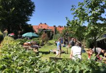 Stöbern und Verhandeln auf Hamburgs Flohmärkten Im Vordergrund steht eine Hecke. Dahinter stehen Menschen, die sich Flohmarkt-Stände ansehen.