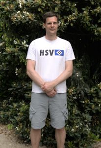 Leichtathletik beim HSV: Leistungssport-Koordinator Nils Lillie steht vor einem Gebüsch.