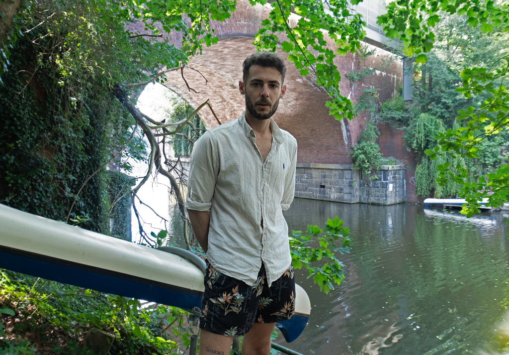 Ein Mann steht vor einem Kanal mit einer Brücke im Hintergrund.