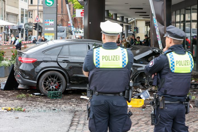 Verkehrsunfall am Jungfernstieg: Polizisten stehen an einem demolierten Auto vor einer Sparkasse in der Hamburger Innenstadt. Ein Auto ist in Hamburg in eine Sparkasse gefahren, es gab mehrere Verletzte.