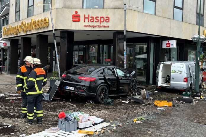 Helfer*innen stehen an einem demolierten Auto vor einer Sparkasse. Ein Auto ist in Hamburg in eine Sparkasse gefahren, es gab mehrere Verletzte.