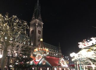 Einhornglühwein, Live-Musik & Winterminigolf Der Weihnachtsmarkt am Hamburger Rathaus am Abend. Im Vordergrund stehen mit Lichterketten beschmückte Buden. Foto: Lara Kitzinger