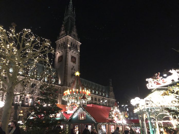 Der Weihnachtsmarkt am Hamburger Rathaus am Abend. Im Vordergrund stehen mit Lichterketten beschmückte Buden. Foto: Lara Kitzinger