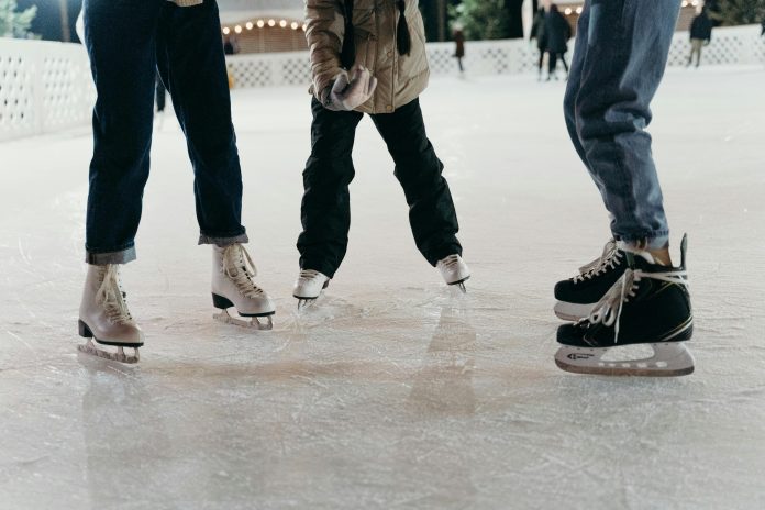 Menschen stehen mit Schlittschuhen auf einer Eisbahn.